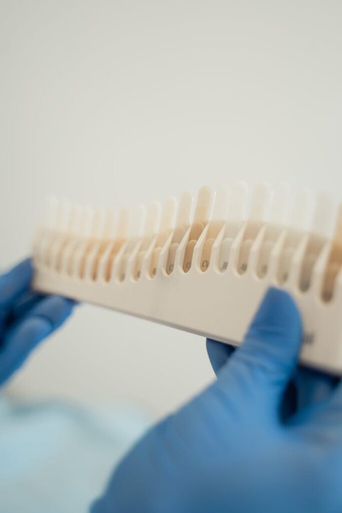 Blue gloved hands holding a dental shade guide in a dental clinic setting.